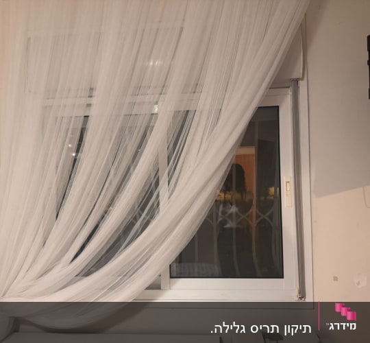 חלון הזזה מאלומיניום לבן מוסתר בחלקו על ידי וילון